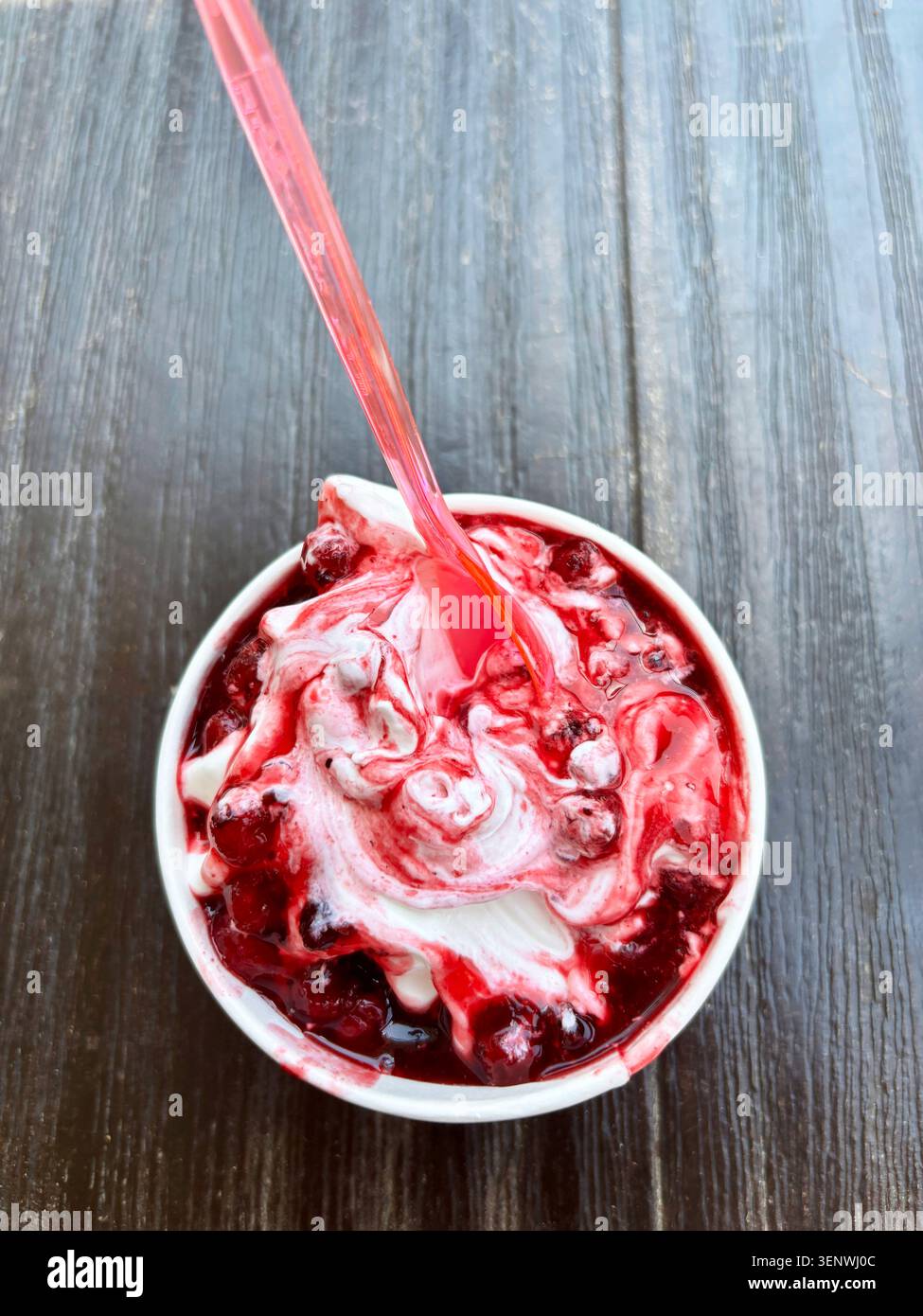 Tazza di yogurt congelato servito morbido con salsa dolce mista di frutti di bosco isolata su un tavolo di legno. Vista dall'alto. Foto Stock
