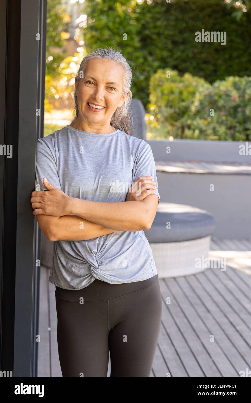 Donna anziana in piedi sul ponte di legno vicino al palo della porta, lounge, con top grigio legato, leggings scuri Foto Stock