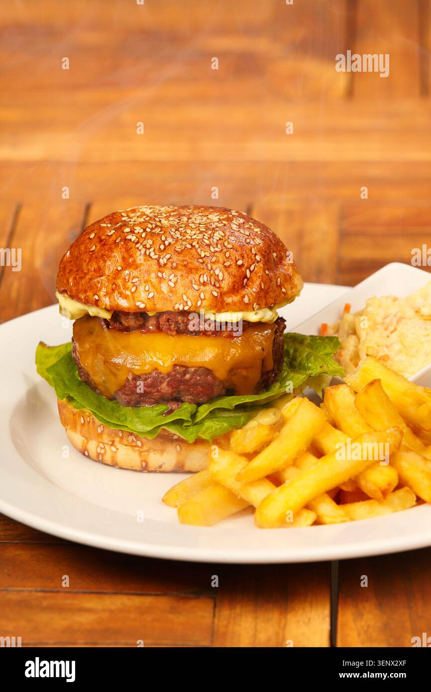 Hamburger di manzo di lusso in panino con formaggio, marmellata di pancetta, lattuga, patatine fritte e insalata di cavolo Foto Stock