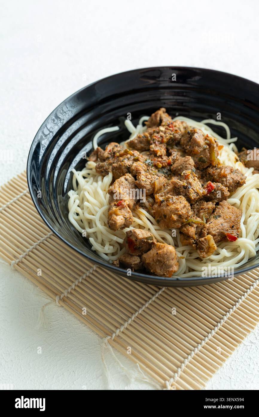 Primo piano di saporiti spaghetti di manzo coreano con semi di sesamo in un recipiente di ceramica nera Foto Stock