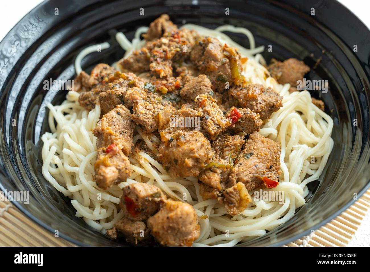 Primo piano di saporiti spaghetti di manzo coreano con semi di sesamo in un recipiente di ceramica nera Foto Stock