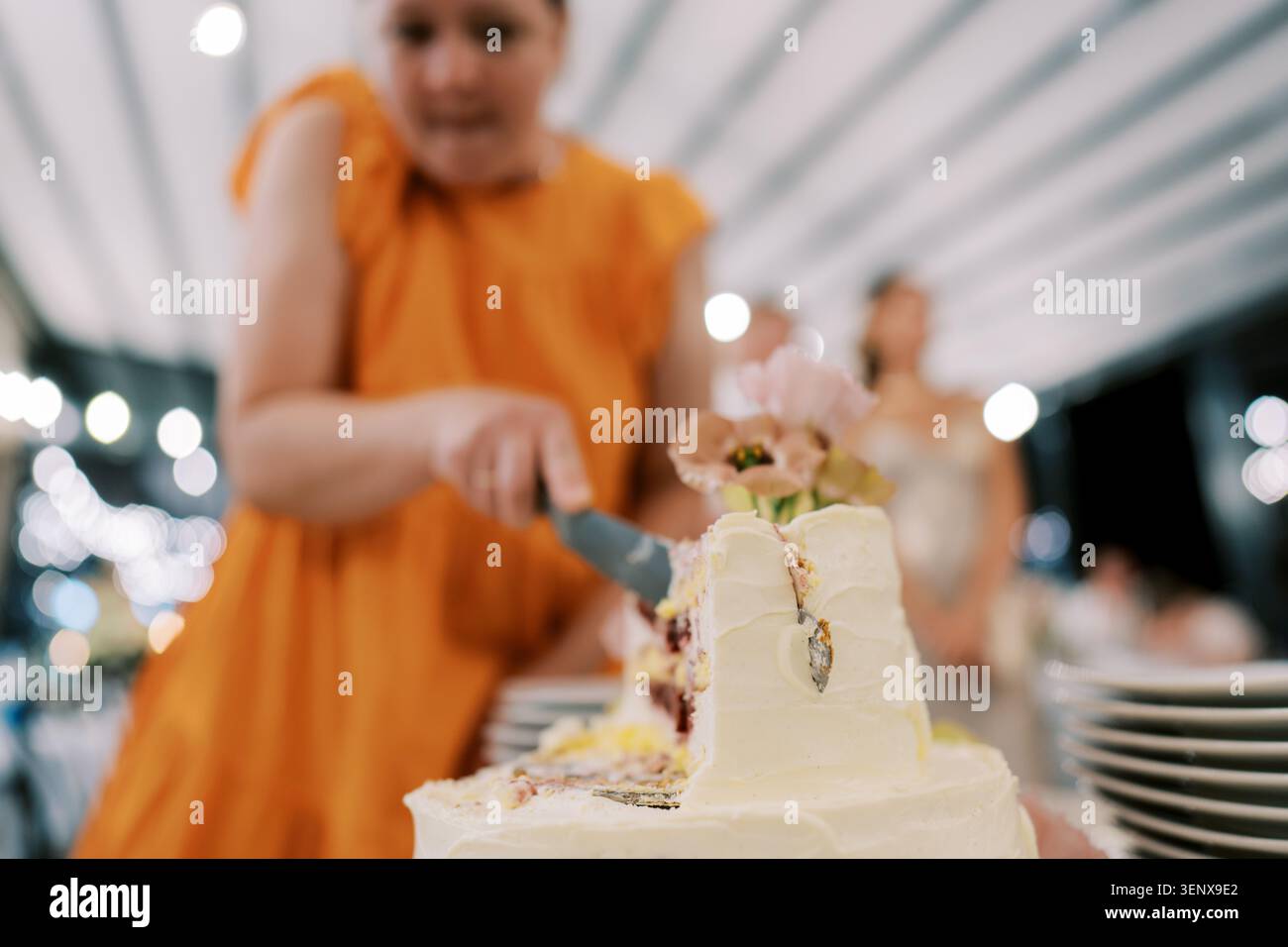 Donna in abito arancione che taglia la torta nuziale Foto Stock