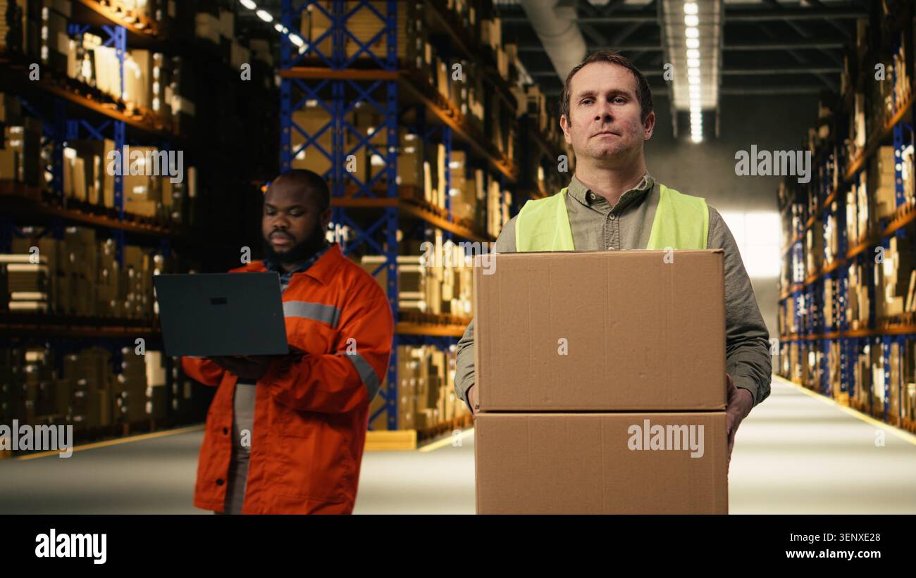 Uomo membro del personale che trasporta scatole e controlla i dettagli del carico nel deposito industriale. Il personale del centro logistico coordina l'evasione degli ordini con la consegna espressa, preparando l'ordine per l'e-commerce. Foto Stock