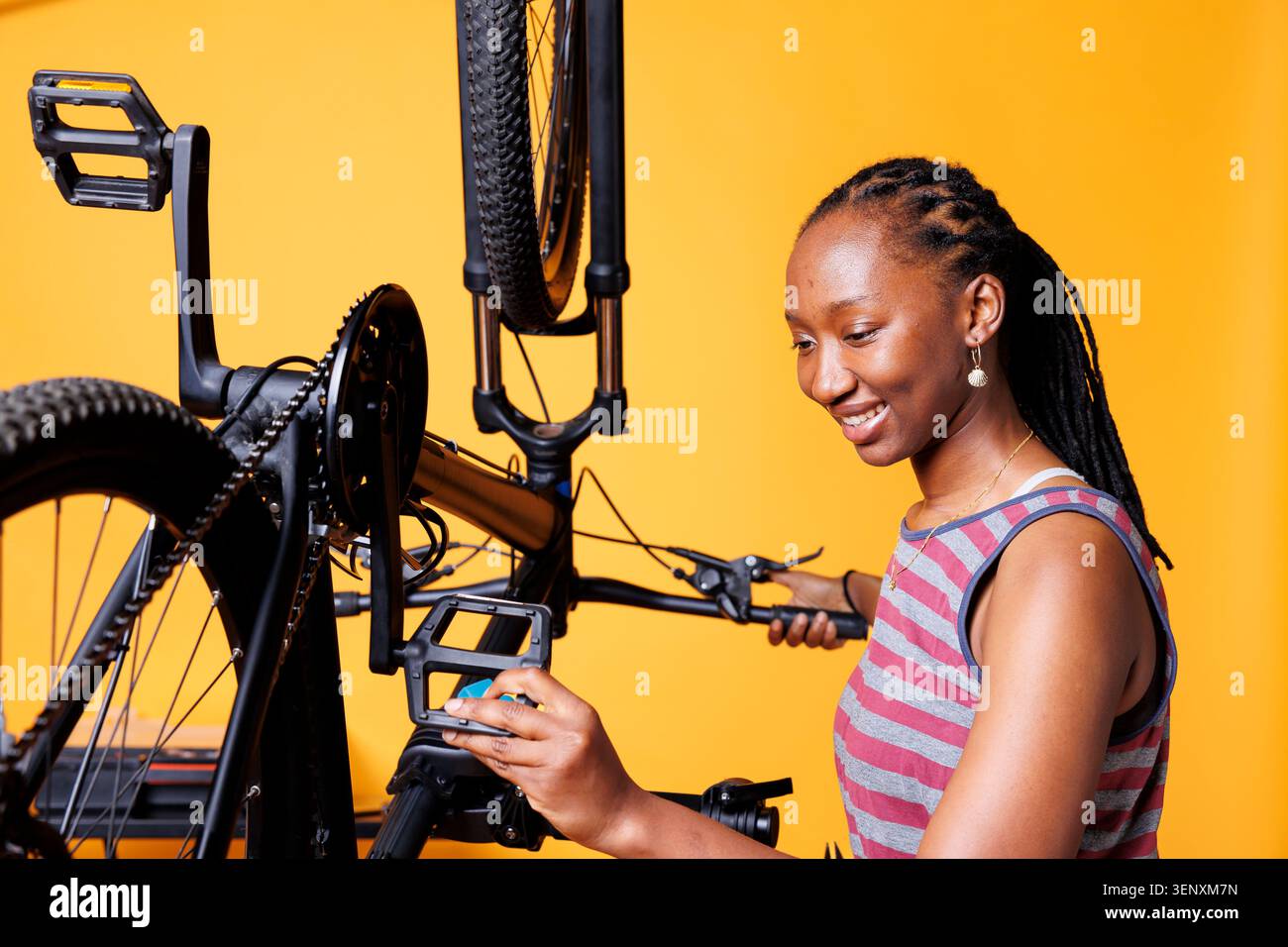 Donna dedicata che esegue la manutenzione della bicicletta per il tempo libero in bicicletta, con una donna sana entusiasta che ispeziona e fissa il pedale della bicicletta che esegue le regolazioni annuali su sfondo isolato. Foto Stock