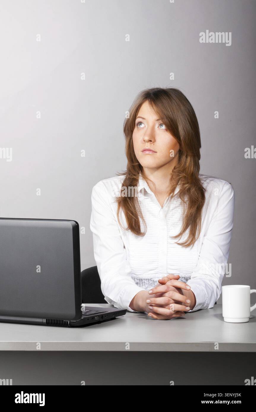 Una donna d'affari è seduta in ufficio con un computer portatile e guarda con attenzione lateralmente Foto Stock