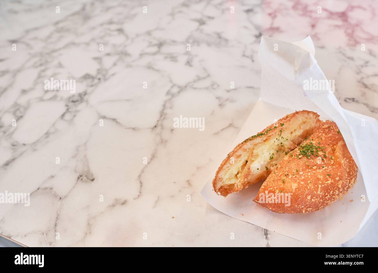 Crocchette di patate croccanti a metà in un involucro di carta bianca su un elegante tavolo in marmo. L'ampio spazio negativo a sinistra è perfetto per il testo pubblicitario. Foto Stock