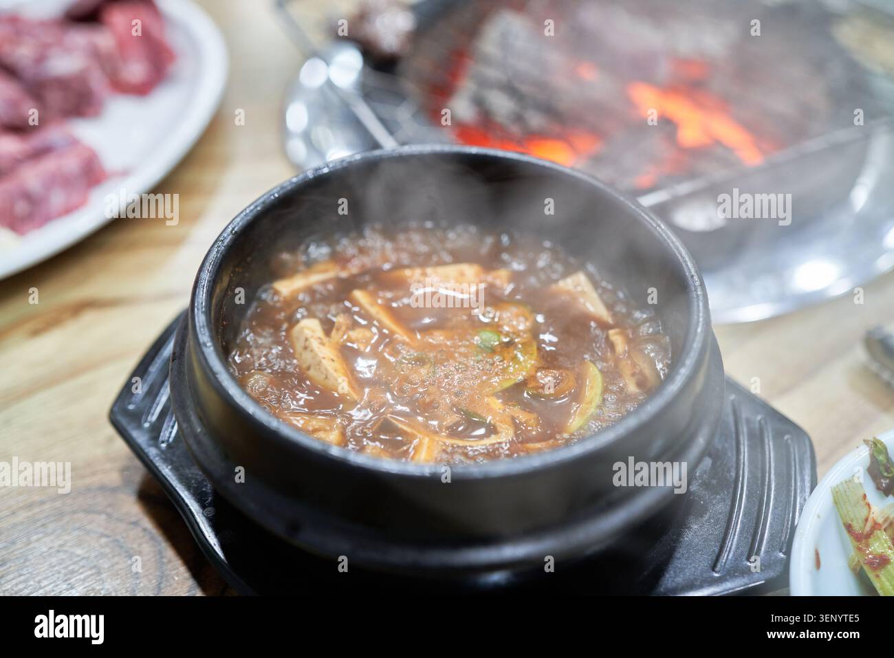 Bollente stufato di pasta di soia in una pentola scura e un cucchiaio d'argento che solleva il tofu di riso bianco e il manzo arrosto, mostrando il perfetto completamento dei pasti asiatici al barbecue di oggi Foto Stock