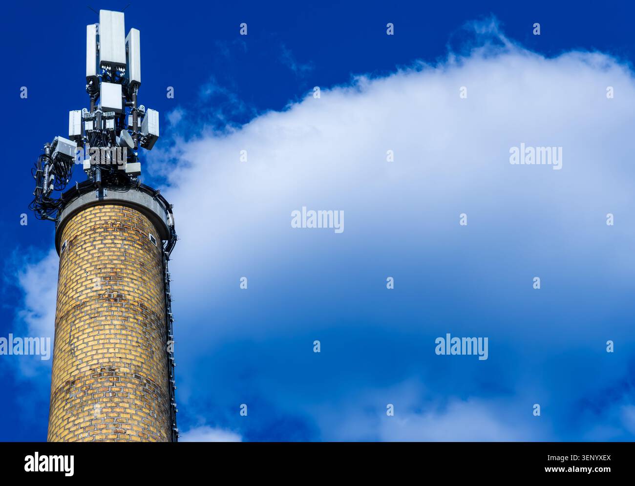 Moderne antenne di comunicazione cellulare 5G montate su uno storico camino in mattoni contro un cielo blu spettacolare con ampio spazio per le copie. Montante 5G, antenna 5G. Foto Stock