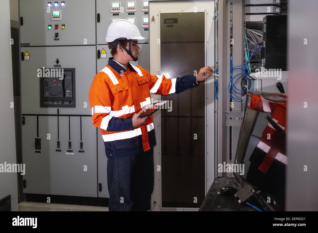 Giovane ingegnere INFORMATICO asiatico in uniforme che utilizza tablet e punta a cavi blu. Ispezione del data center di rete dei rack server, manutenzione delle telecomunicazioni Foto Stock
