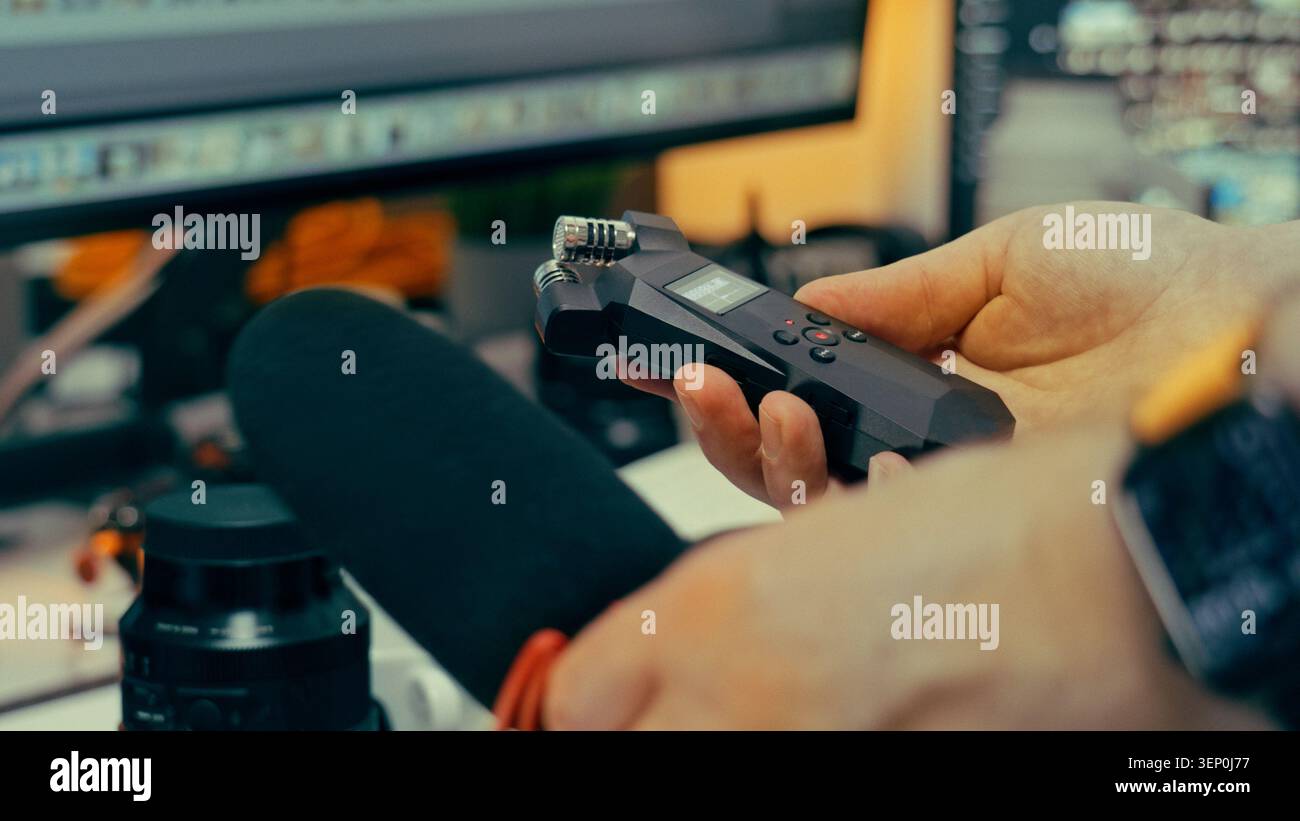 Le mani del creatore tengono in mano il registratore audio digitale il microfono esterno la workstation del monitor dello studio. Un sound designer regola le impostazioni su un dispositivo portatile Foto Stock