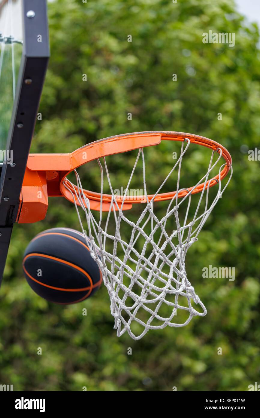 Pallacanestro nero che colpisce Orange Hoop e rete all'aperto contro Green Trees Foto Stock