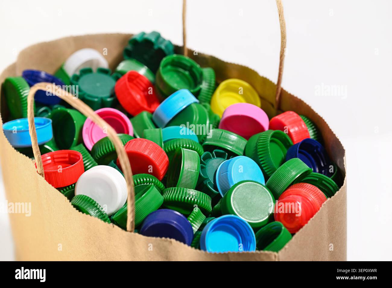 Sacchetto di carta riempito con tappi colorati in plastica. Simbolo della separazione dei rifiuti e dello smistamento sostenibile delle materie plastiche. Foto Stock