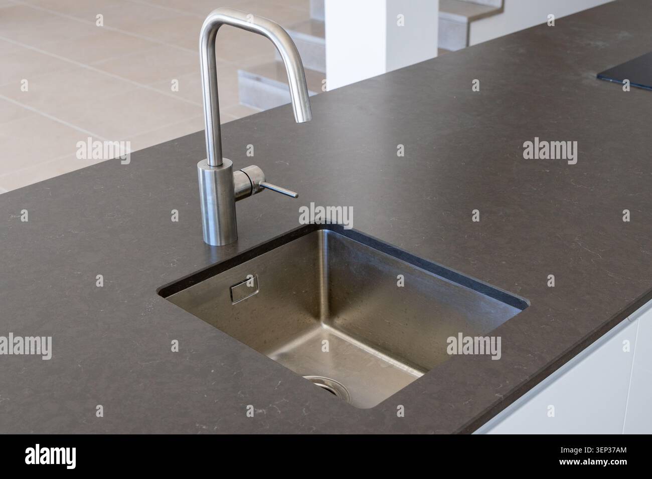 Un'isola di cucina contemporanea presenta un profondo lavandino in acciaio inossidabile e un rubinetto cromato minimalista, perfetto per un design moderno della casa Foto Stock