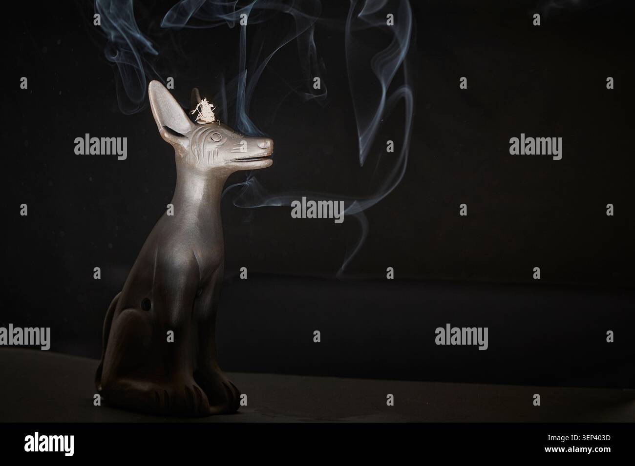 Antica statua egiziana dello sciacallo anubi in piedi con fumo di incenso bianco arricciato su sfondo scuro Foto Stock