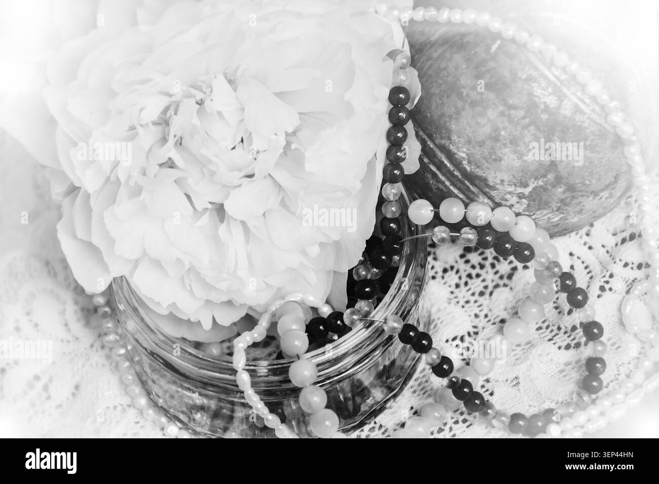 Sfondo vintage con peonia rosa, gioielli in vaso di vetro e vecchia palla di ferro arrugginita sul pizzo. Luce soffusa. Foto obsoleta. Bianco e nero. Foto Stock