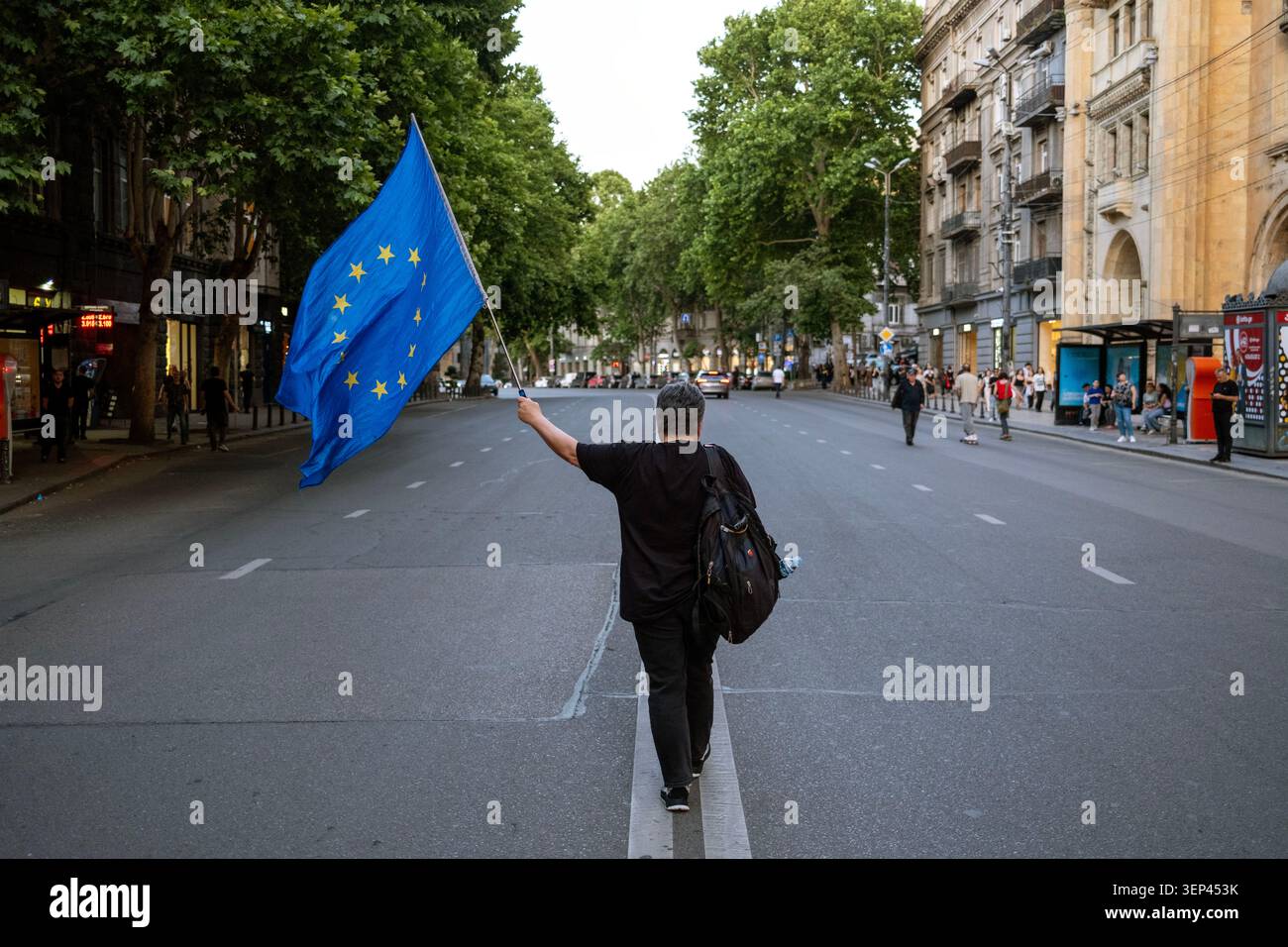 Tbilisi, Georgia, 13 giugno 2026. Una donna batte la bandiera dell'Unione europea mentre lei e altri manifestanti partecipano al 563° giorno di manifestazioni anti-governative a Tbilisi. Foto Stock