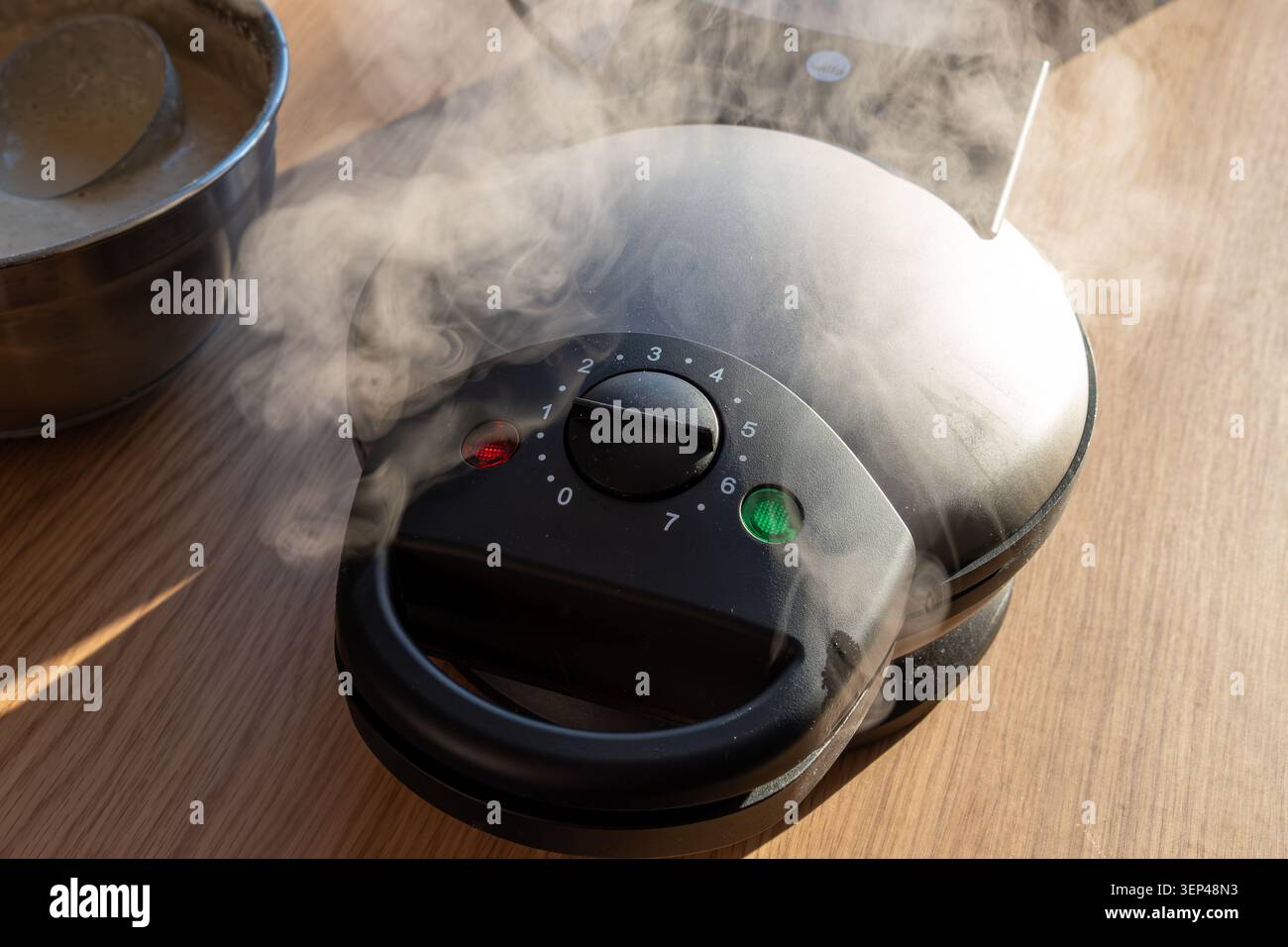 Ferro da stiro elettrico per preparare waffle con vapore e ciotola di impasto per waffle sotto la luce calda del sole Foto Stock