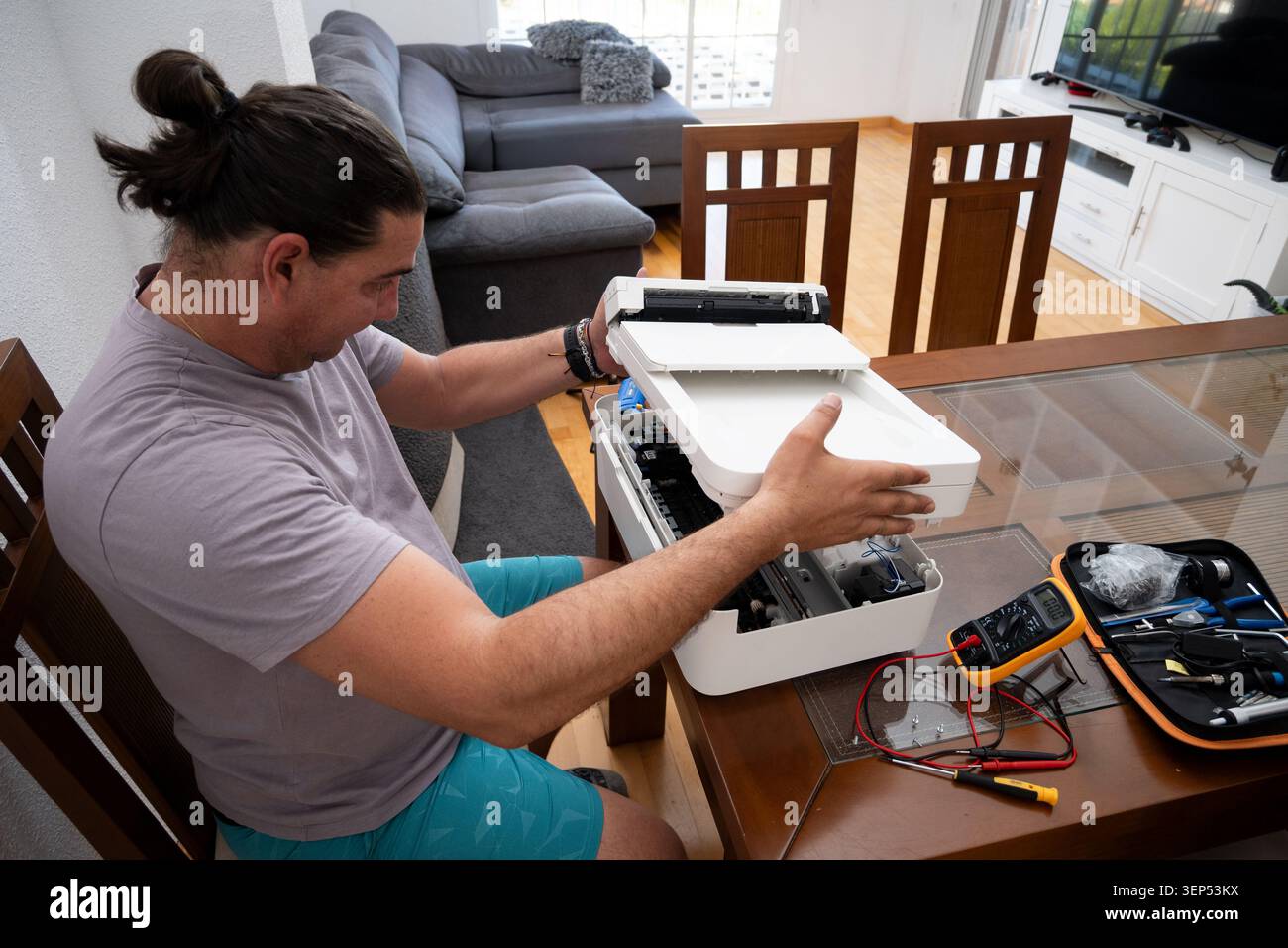 Uomo risoluzione dei problemi e riparazione della stampante personale a casa utilizzando vari strumenti Foto Stock