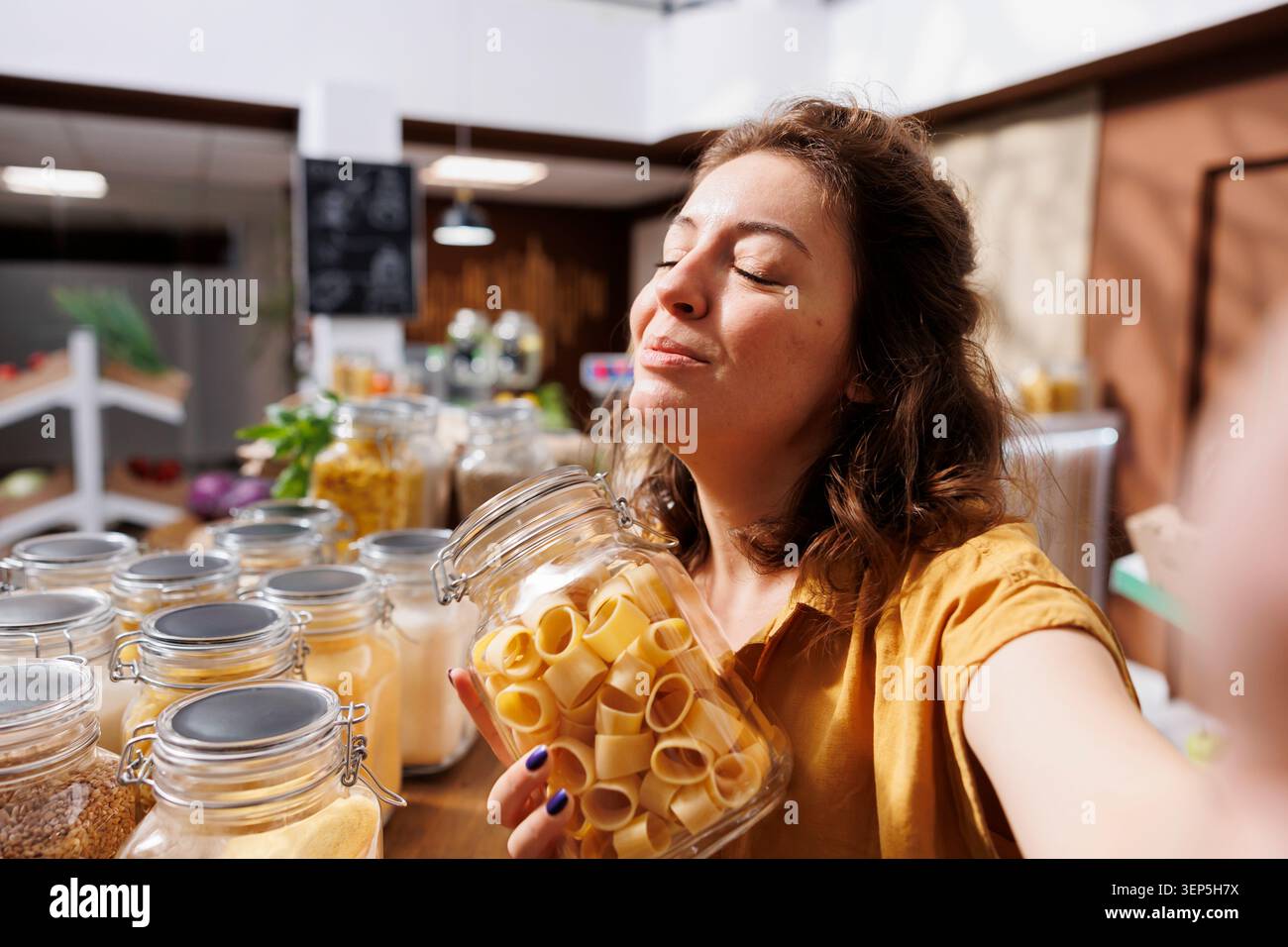 Influencer che realizza video su Internet per i social media, presenta un negozio ecologico a rifiuti zero mentre vlogger per uno stile di vita sostenibile si riprende all'interno di un negozio di alimentari locale di prodotti sfusi. Foto Stock