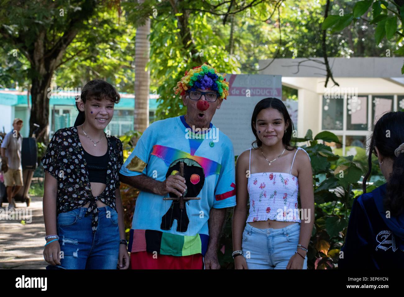 Un artista colorato vestito da clown che posa con due ragazze in un parco all'aperto a Ciego de Avila, Cuba Foto Stock