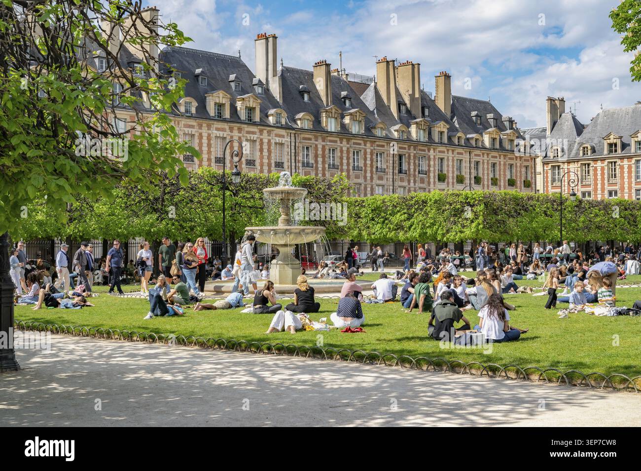 Vivace parco di Piazza Luigi XIII nella storica Place des Vosges con gente del posto e turisti sui prati vicino a una fontana di fronte all'elegante baroq Foto Stock