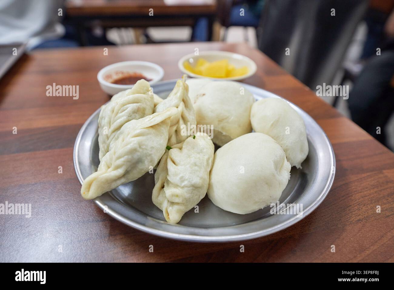 Il tradizionale cibo di strada asiatico presenta salate tasche di pasta ripiegate e panini bianchi su un piatto d'argento con ravanello sottaceto su questo tavolo di legno. Foto Stock