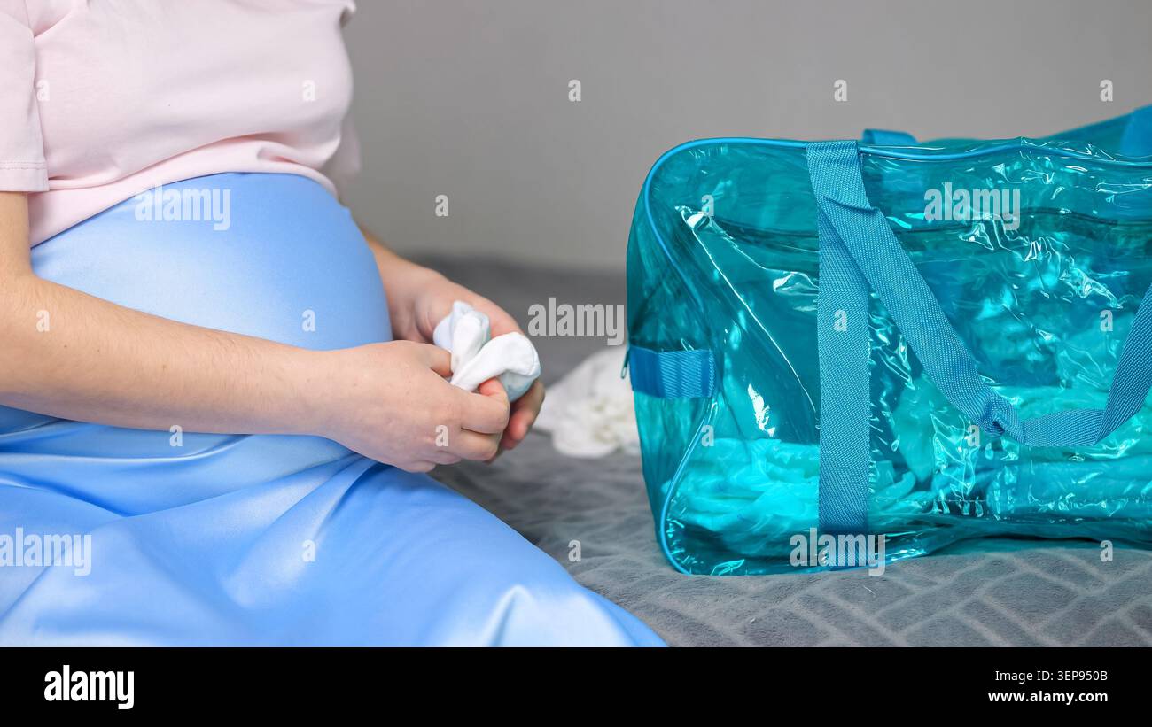 Donna incinta che imballa vestiti del bambino per la borsa dell'ospedale Foto Stock