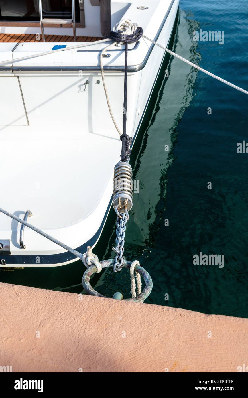 Uno yacht è fissato a un molo utilizzando funi multiple, una catena di metallo e una sorgente di ormeggio in acciaio inossidabile sopra acque verdi profonde. Foto Stock