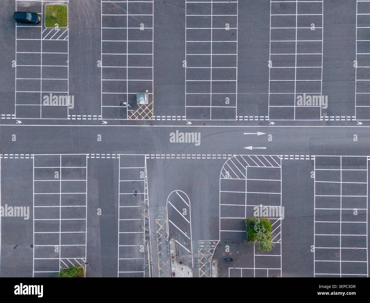 Prospettiva dall'alto di un parcheggio organizzato con numerosi parcheggi vuoti e frecce direzionali dipinte su asfalto scuro Foto Stock