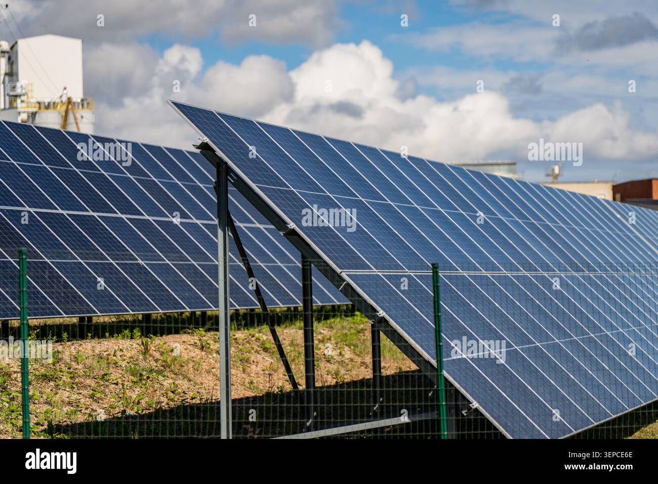 Moderni array di celle solari che catturano energia alternativa su un terreno di campo tramite una recinzione di sicurezza che rappresenta infrastrutture elettriche e powe ecologiche Foto Stock