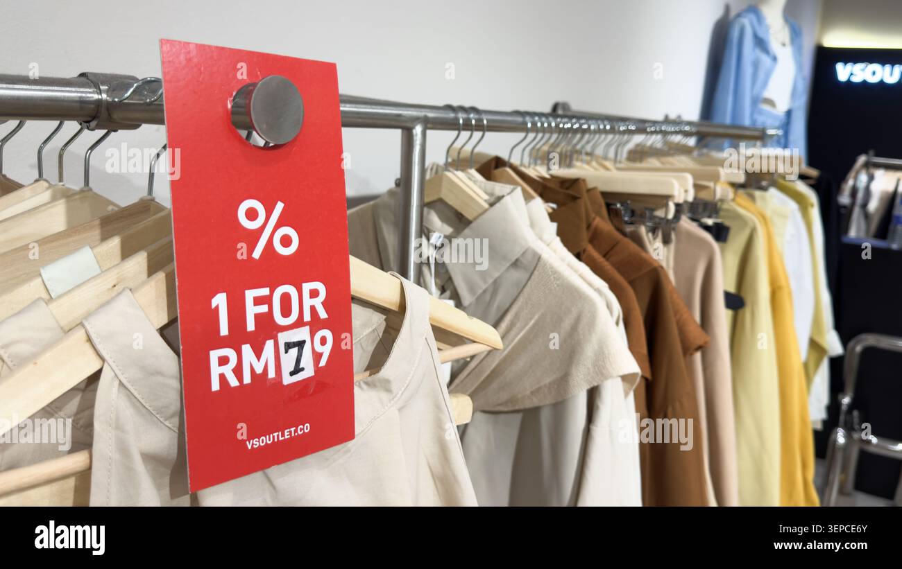 Penang, Malesia - 18 aprile 2025: Un'esposizione al dettaglio presenta un cartello promozionale che indica una vendita di abbigliamento, che mostra vari capi appesi al rac Foto Stock