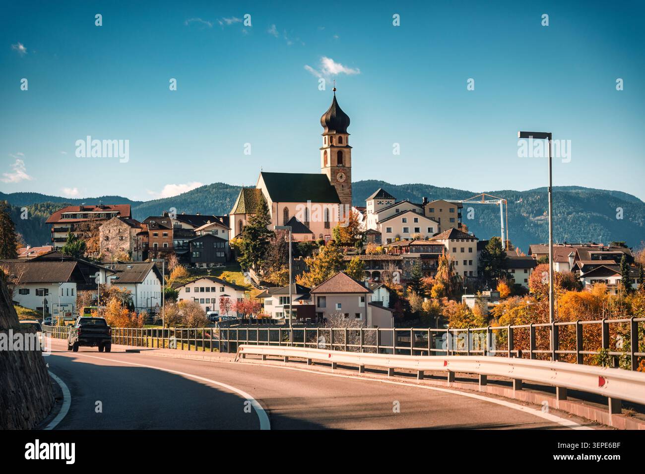 Pittoresca chiesa cattolica storica con campanile circondata da colorate foglie autunnali e tradizionale villaggio di architettura alpina sulla collina sotto B. Foto Stock