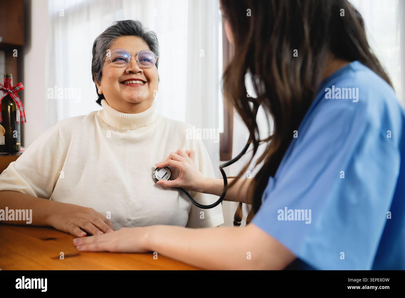 Giovane infermiera che controlla il cuore anziano donna stetoscopio, esaminando anziani paziente battito cardiaco in casa accogliente, felice signora in pensione che riceve il controllo medico lui Foto Stock