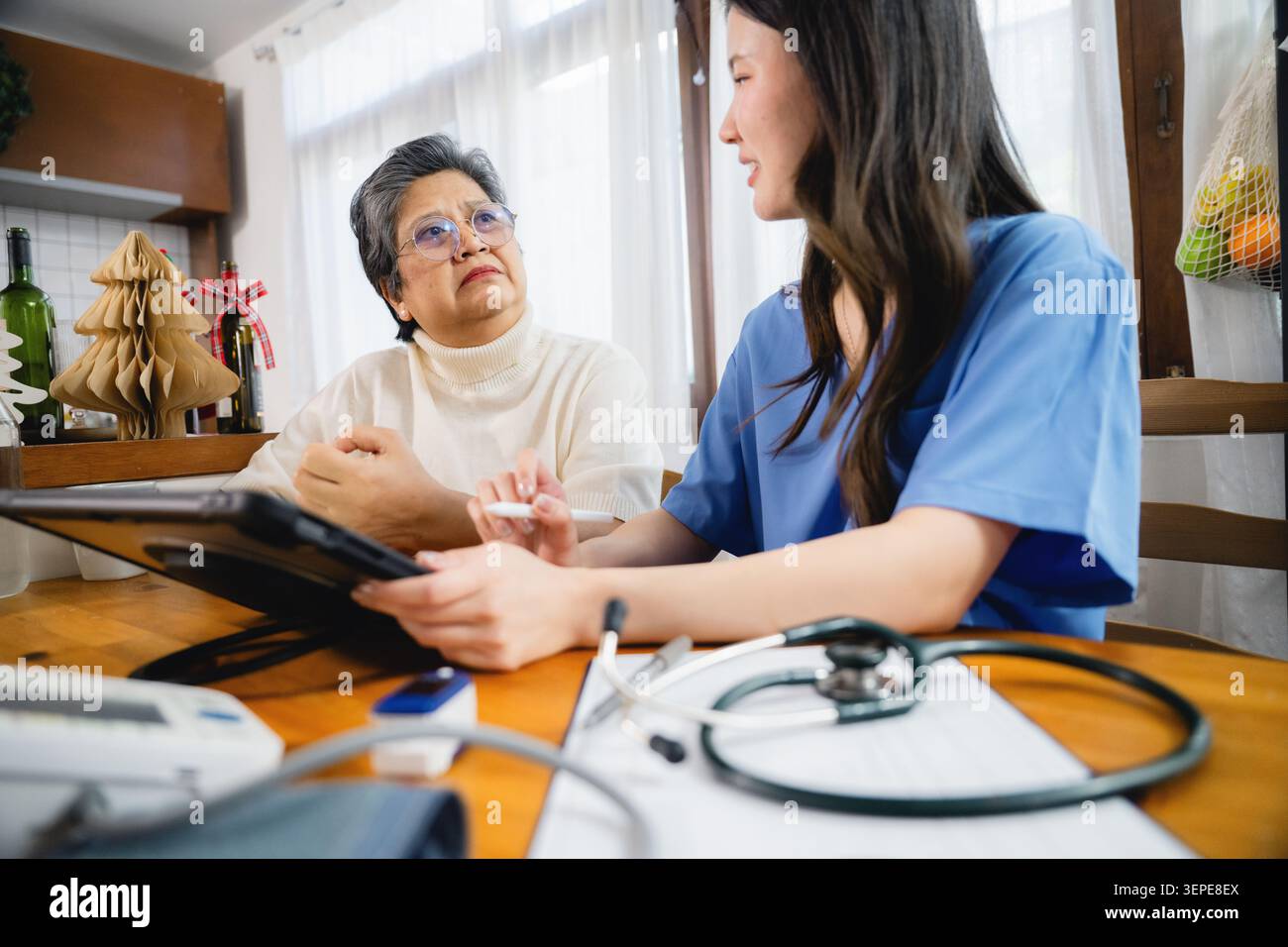 Grave donna asiatica senior sta ascoltando infermiera spiegare come utilizzare la tecnologia tablet in consultazione con i dispositivi medici in primo piano. discutere di guarigione Foto Stock