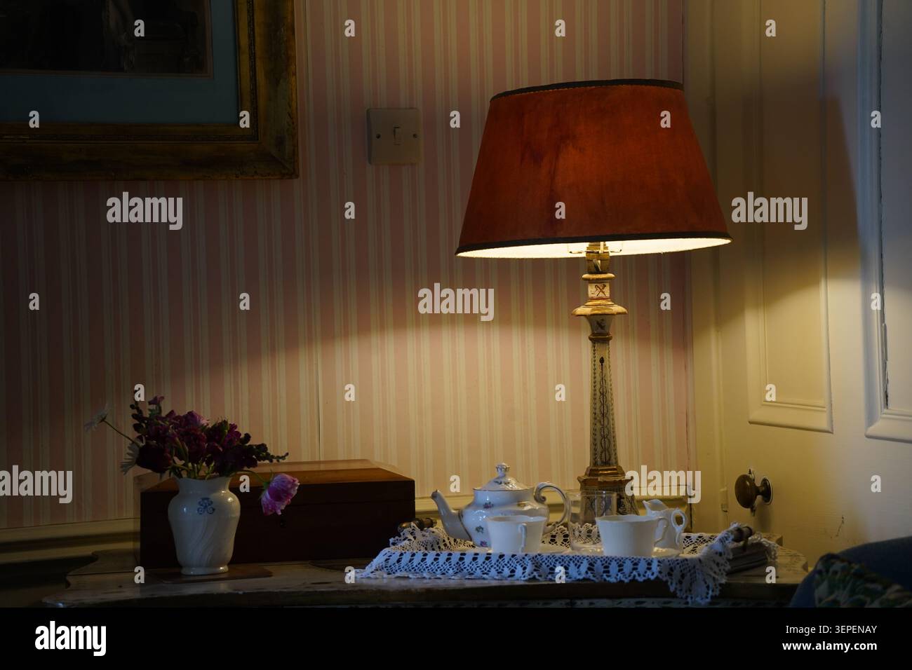 Un intimo set da tè vintage disposto sotto una calda lampada da tavolo Foto Stock