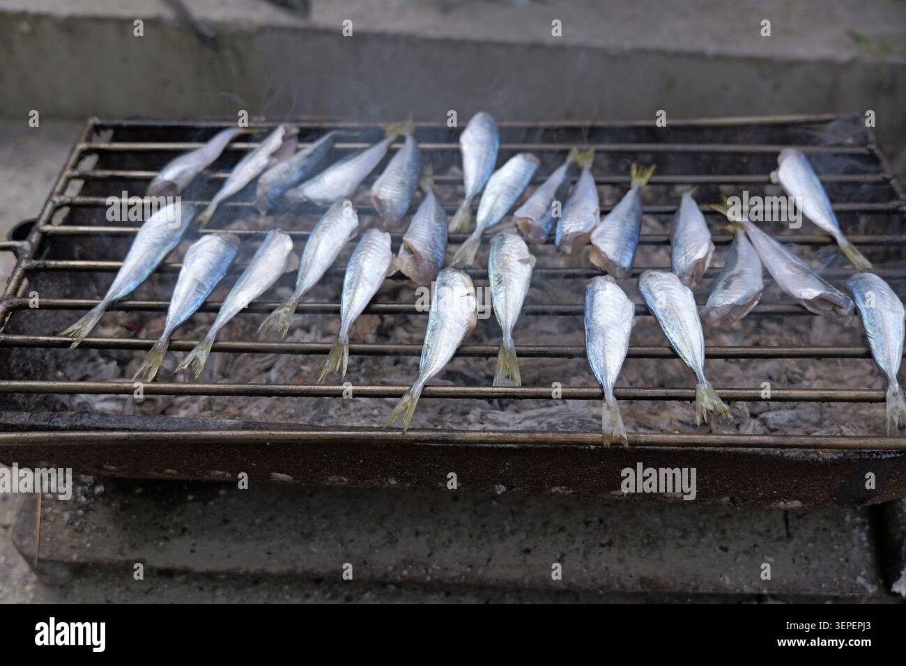 Pesce intero fresco grigliato su carbone caldo, fumo che si arriccia mentre le fiamme bruciano la pelle per un rustico pasto barbecue all'aperto, perfetto per raduni estivi Foto Stock