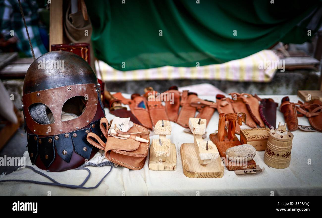 Tallinn, Estonia - 11 luglio 2025: Un casco medievale, pelletteria e artigianato in legno sono esposti su un tavolo al mercato dei giorni medievali Foto Stock