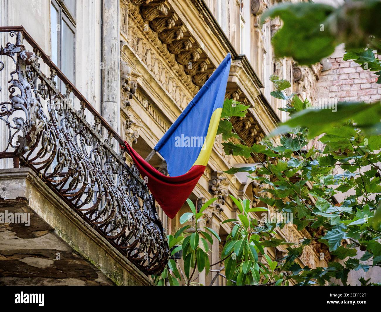 Bandiera rumena sul balcone ornato in ferro battuto di un edificio Beaux-Arts a Bucarest (Bucuresti), Romania. Foto Stock