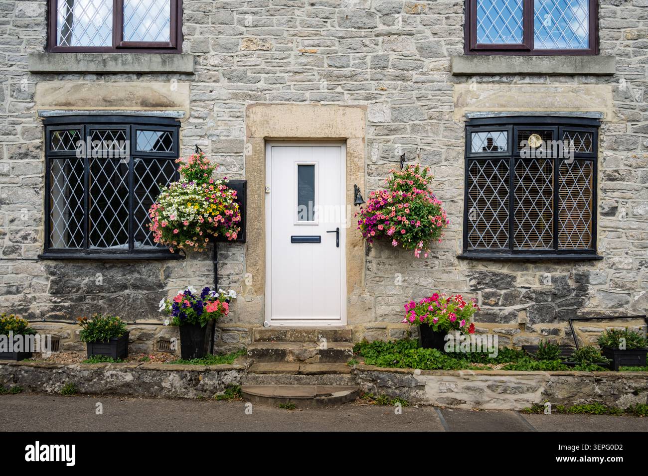 Vista architettonica dettagliata incentrata sulle cornici delle finestre in pietra, finestre in vetro con piombo e cesti di fiori appesi di un tradizionale cottage in pietra Foto Stock