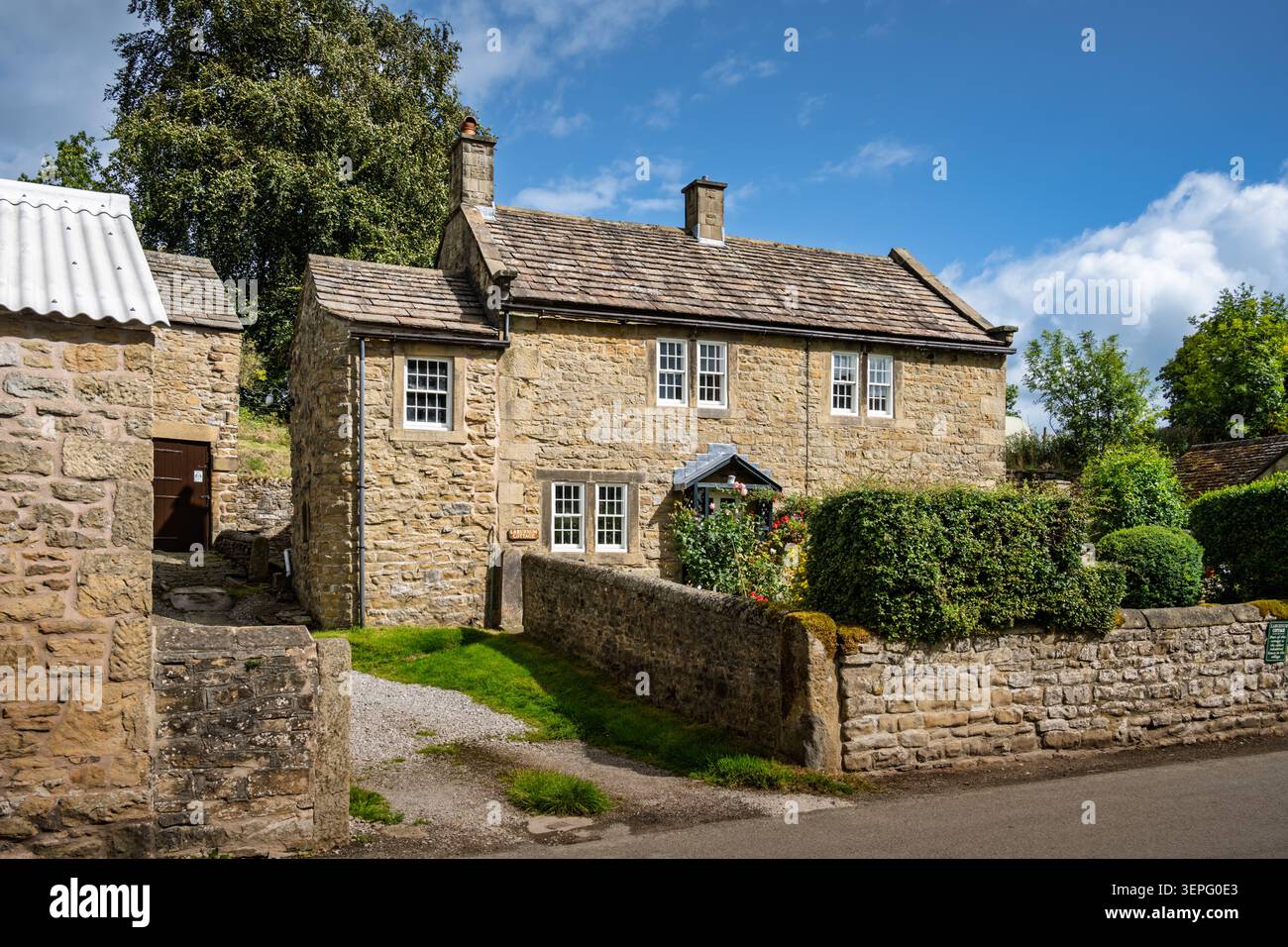Vista a tre quarti dello storico cottage Laburnum costruito in pietra dietro un tradizionale muro di confine in pietra a secco nel villaggio di Eyam, Derbyshire Foto Stock