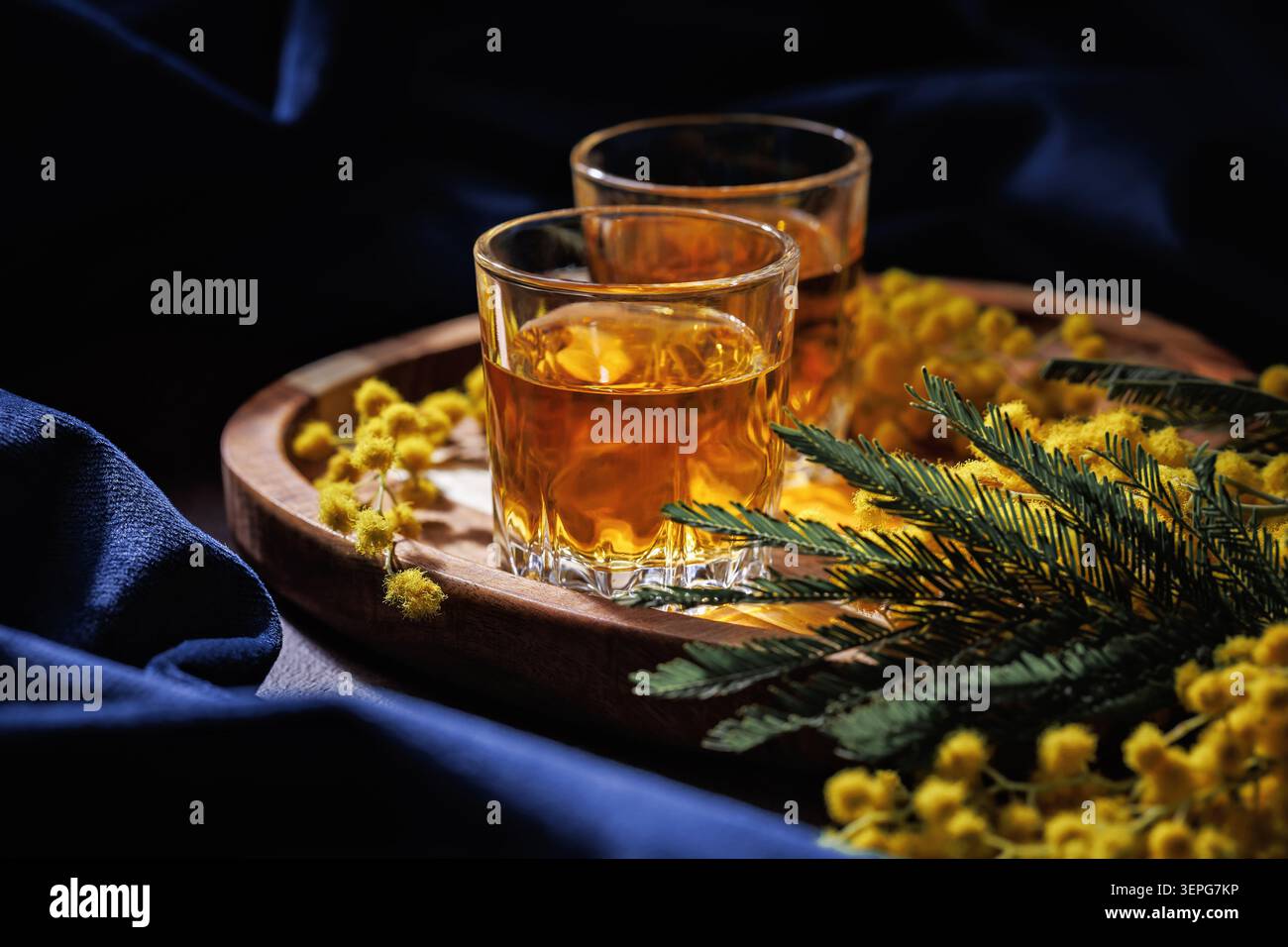 Bicchieri da whisky o Cognac con fiori di Mimosa su vassoio di legno scuro elegante drink Foto Stock