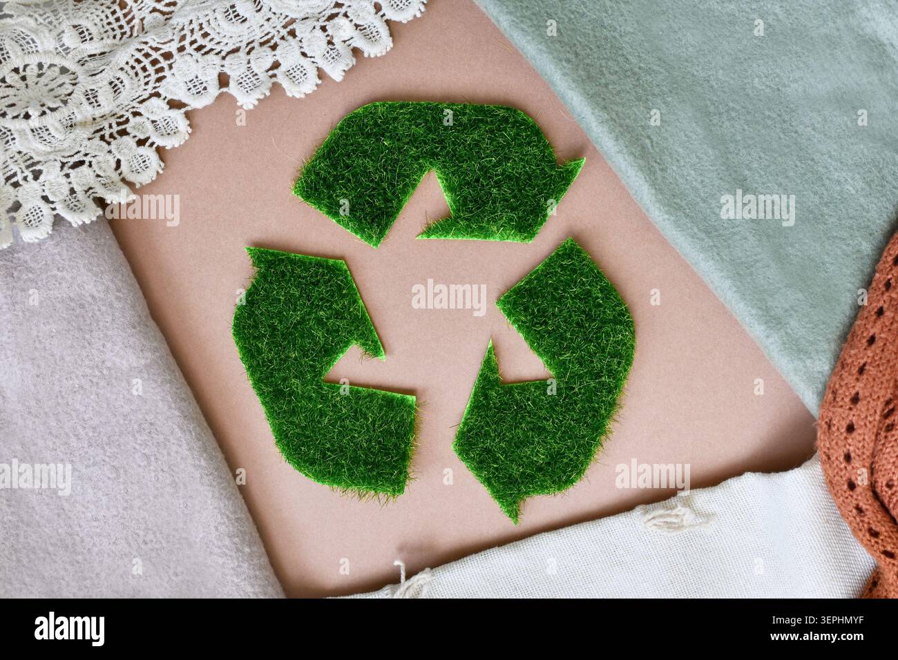 Insegna di riciclaggio fatta di erba verde circondata da tessuti tessili. Moda sostenibile, abbigliamento ecologico e industria tessile naturale Foto Stock