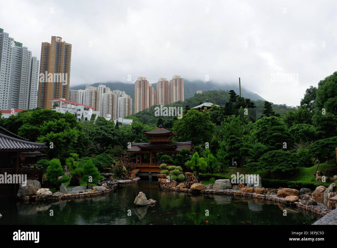 DIAMOND HILL, HONG KONG - 27 LUGLIO 2023: Laghetto con giardino di Nan Lian e padiglione sotto colline nebbiose e grattacieli di Hong Kong. Foto Stock