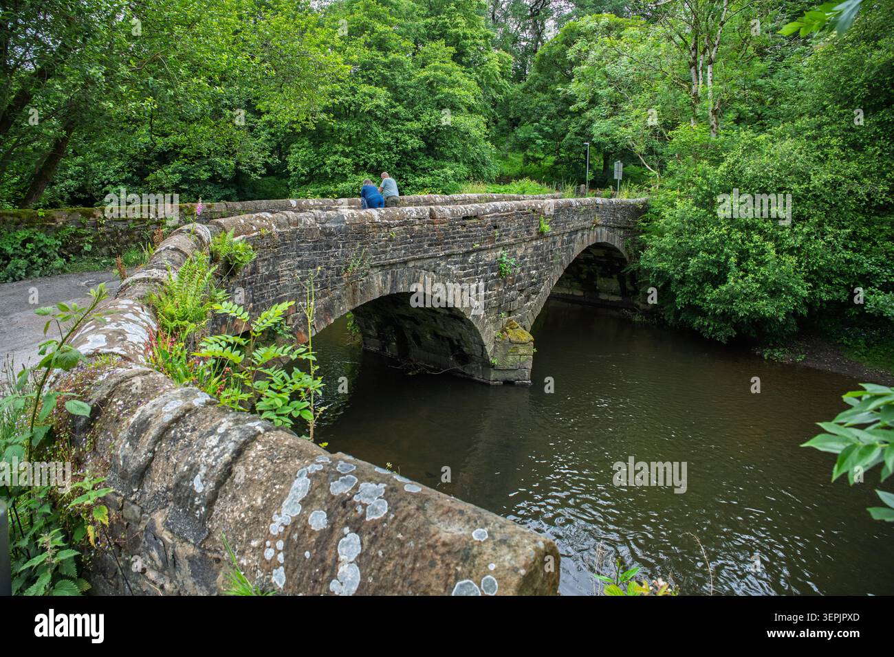 Un paio di persone guardano giù nell'acqua di un fiume da un vecchio ponte di pietra. Foto Stock