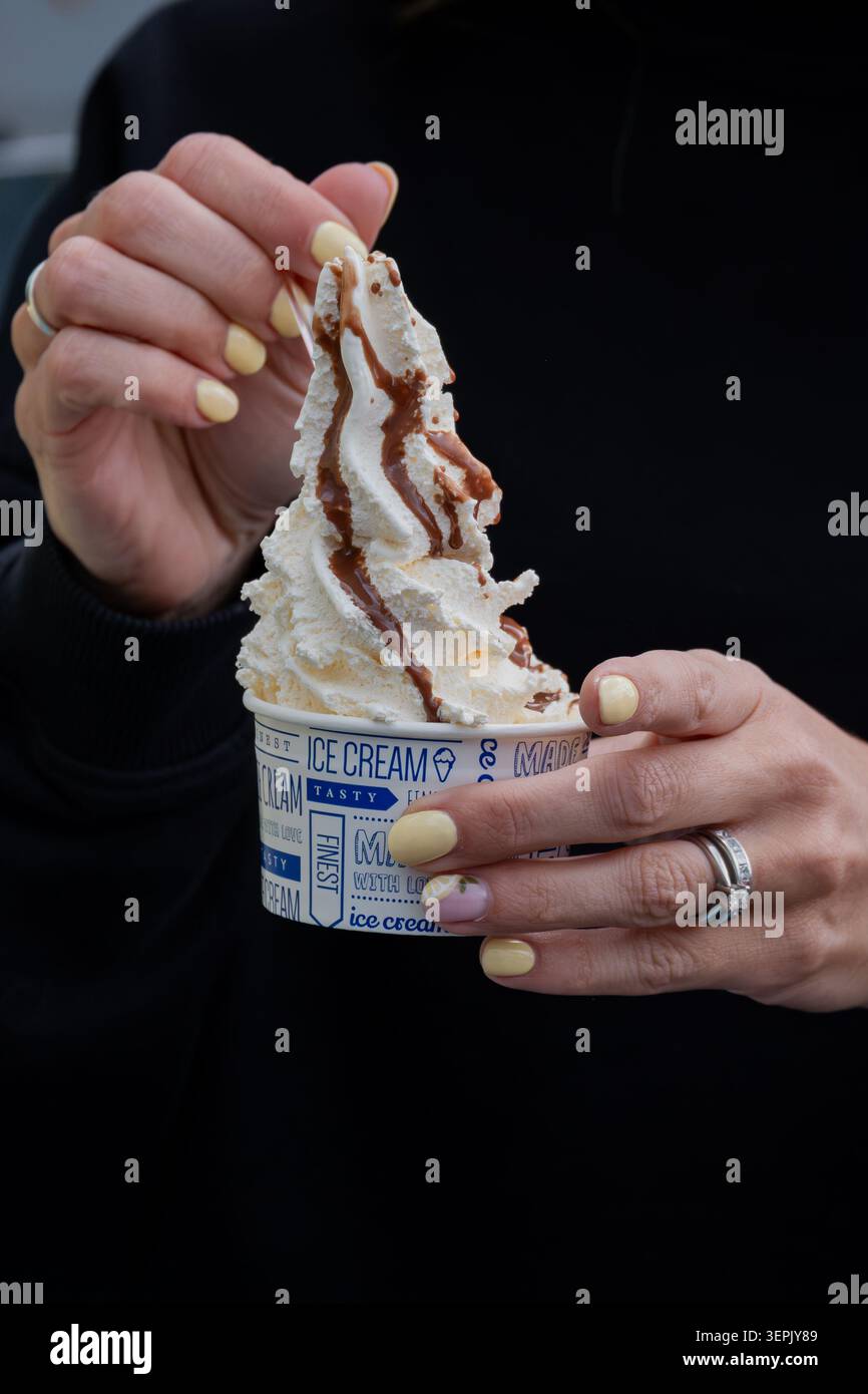 Primo piano di mani che reggono una vasca di gelato montato condita con salsa al cioccolato. Foto Stock