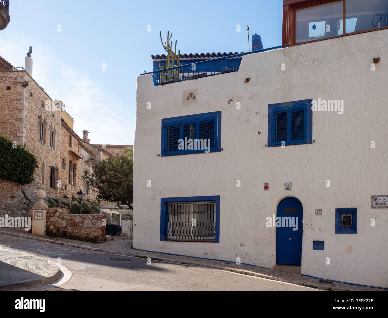 Sitges, Spagna - 20 marzo 2026: Vista sulla strada illuminata dal sole di una classica casa mediterranea con pareti dipinte di bianco e iconiche porte blu e wi-fi Foto Stock