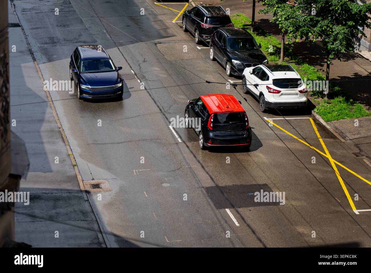 Moderna station wagon blu che guida su strada asfaltata bagnata accanto alle auto parcheggiate in via Gertrudes a riga, ai trasporti urbani e alle infrastrutture stradali cittadine Foto Stock