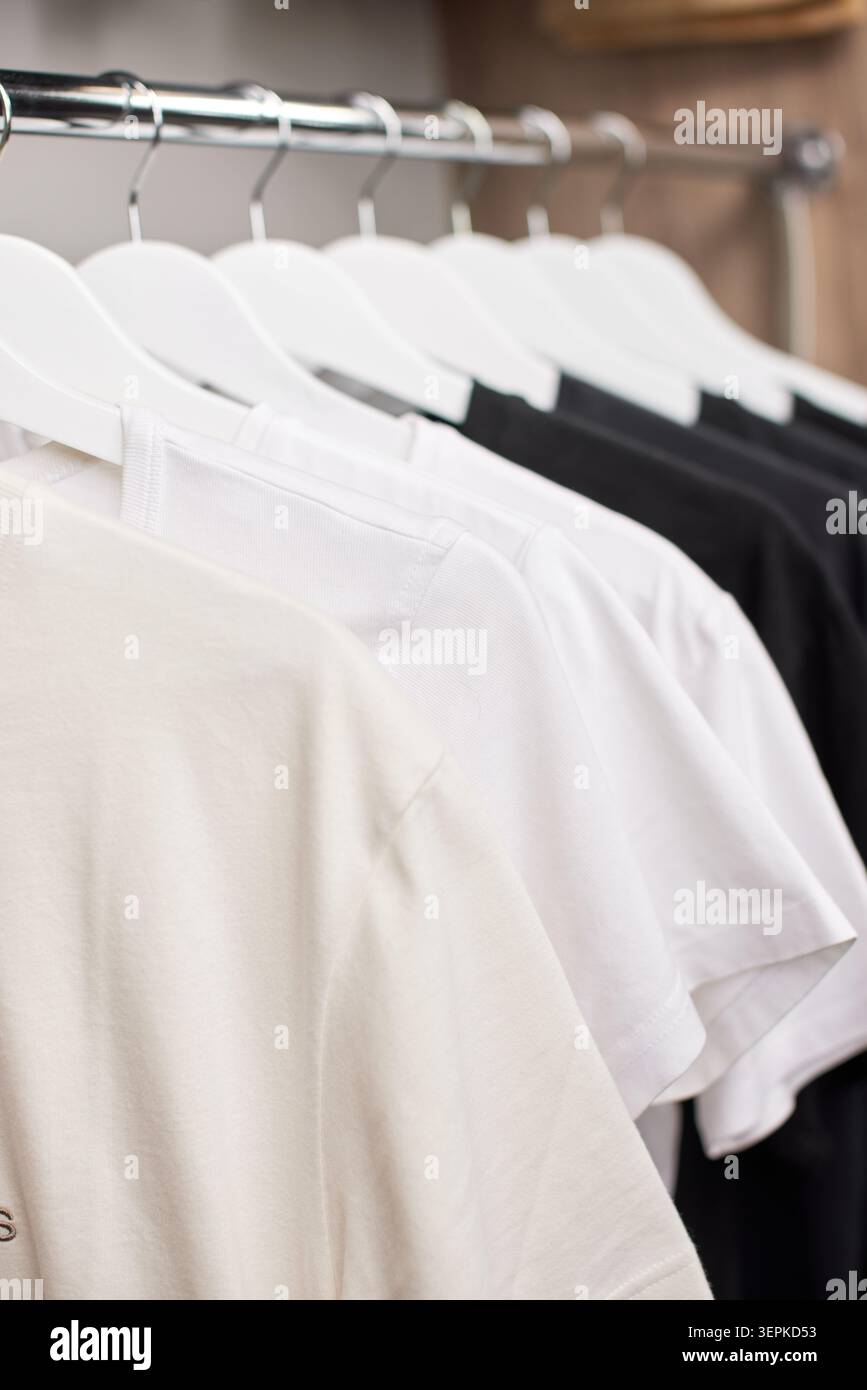 T-shirt bianche e nere appese ordinatamente su appendiabiti in legno bianco in un armadio minimale, creando un'esposizione di abbigliamento organizzata Foto Stock