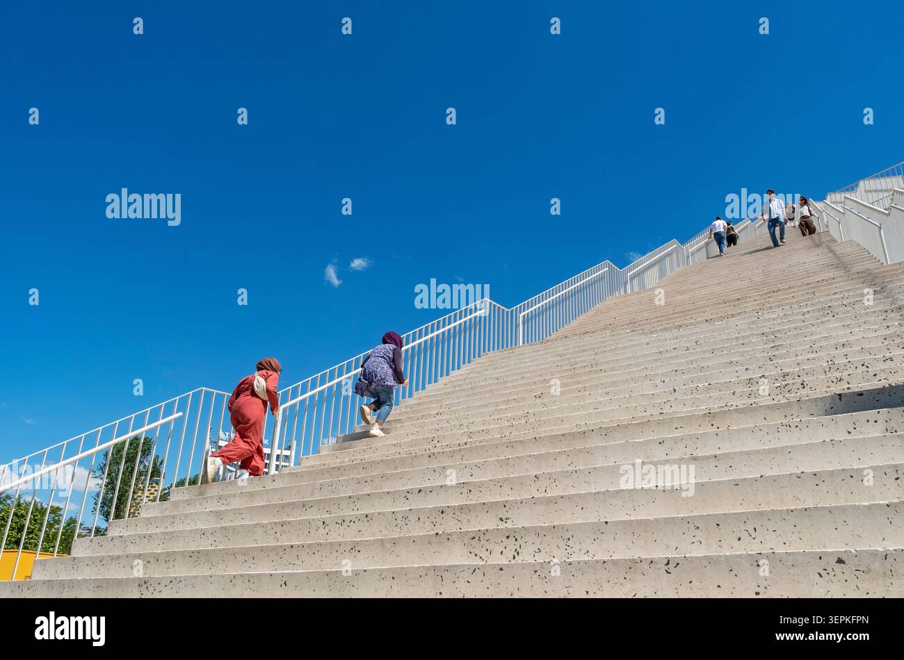Le persone salgono le monumentali scale di cemento che conducono alla rinnovata Piramide di Tirana sotto un cielo blu brillante, l'Albania Foto Stock