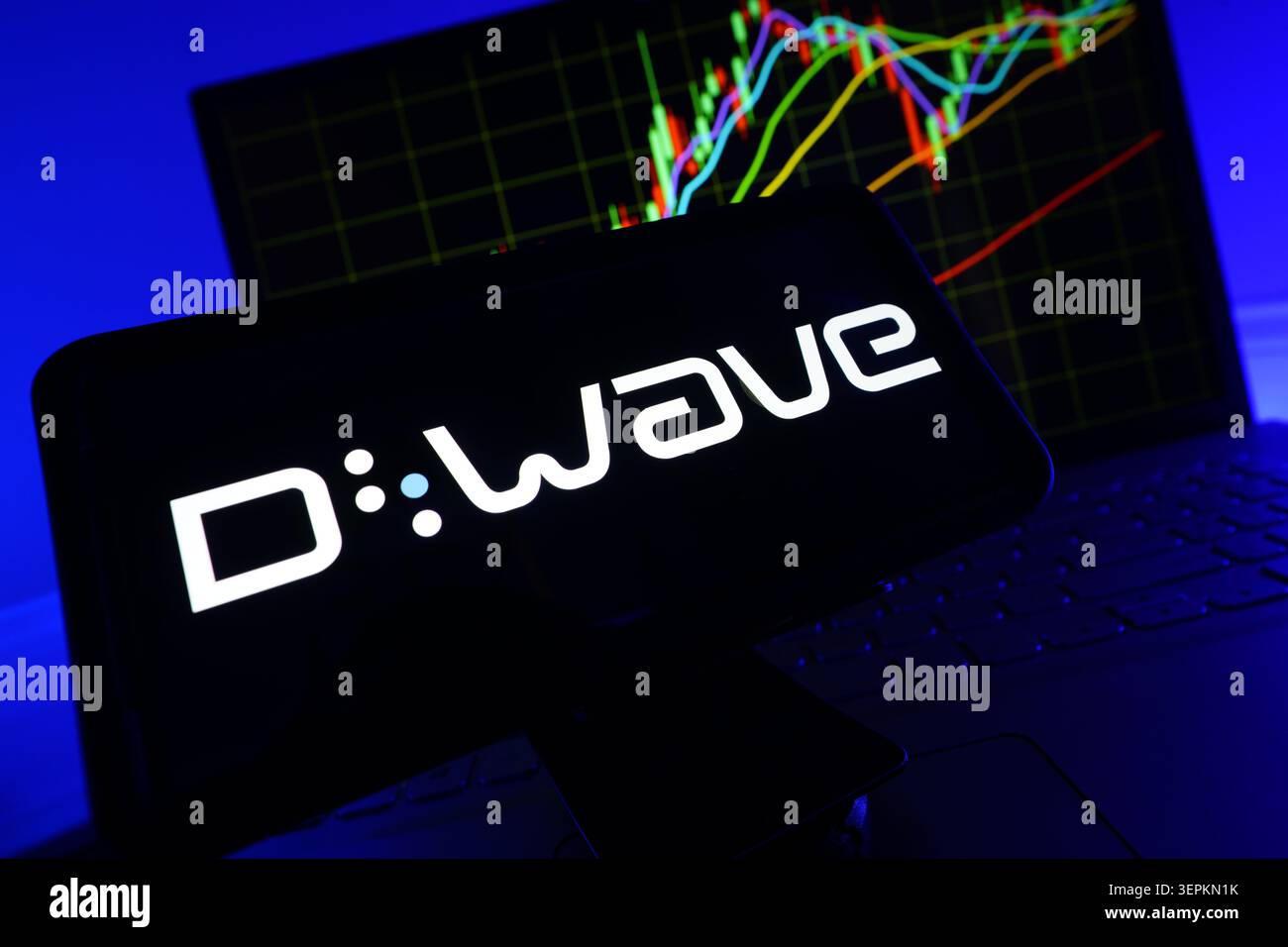 Logo di D-Wave Systems sullo schermo dello smartphone con grafico delle prestazioni del mercato azionario sul computer Foto Stock
